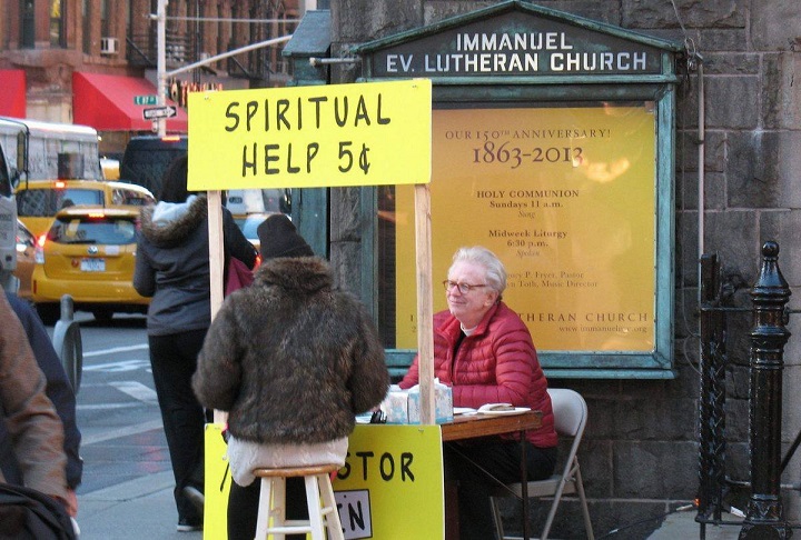 “The Pastor Is In,” reads the sign below the prayer booth that a pastor set up on a sidewalk outside his New York church, and people are stopping by and asking for prayers.